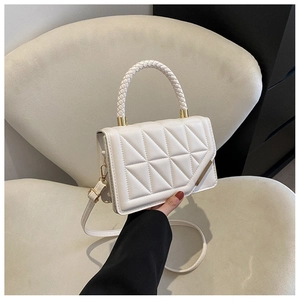 Detail of quilted beige handbag featuring woven handle and gold metal trim on the flap