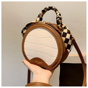 Detail of round handbag featuring crocodile pattern, scarf handle and stitched leather edges