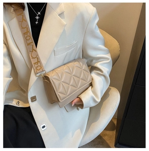 Detail of beige quilted flap bag with patterned wide fabric strap and metal lock closure