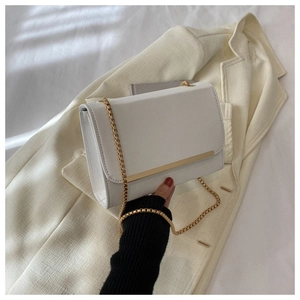 Detalle de bolso bandolera blanco con elegante cadena dorada y adornos metálicos