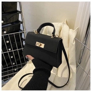 Detail of black matte square handbag with gold metal lock held against a beige blazer