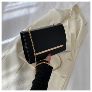 Detalle de bolso bandolera rectangular negro con cadena dorada sobre blazer blanco