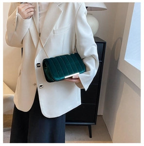 Detail of dark green velvet shoulder bag with vertical quilting and gold chain strap