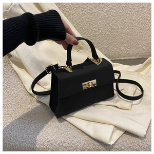 Detail of a black mini square bag featuring a gold twist lock and matte leather texture
