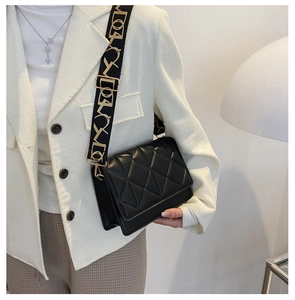 Detail of black quilted leather crossbody bag featuring a wide patterned strap and matte finish
