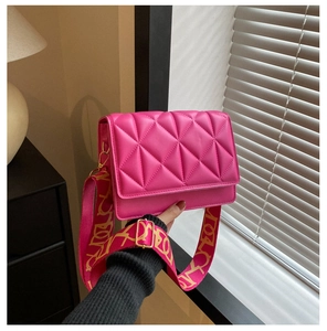 Close-up of bright pink quilted crossbody bag with gold buckle and artistic strap