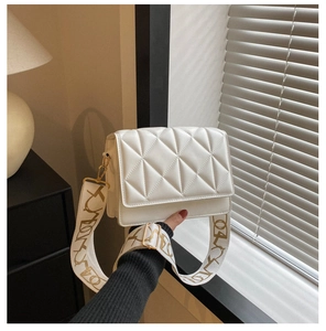 Detail of white quilted handbag featuring a wide textile strap with golden hardware