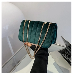 Detailansicht einer Hand, die eine dunkelgrüne Samttasche mit goldener Kette hält