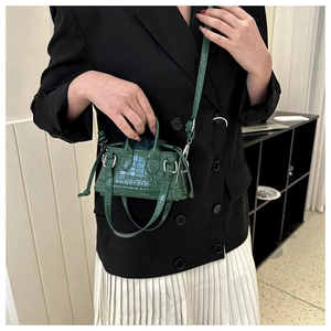 Detail of dark green croc-effect mini bag featuring top handles and fashion embossing