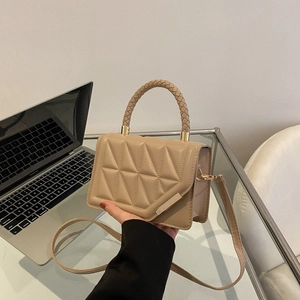 Chic quilted beige crossbody bag with woven handle and gold trim on an office desk
