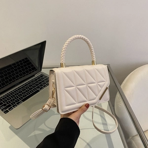 White quilted crossbody bag with woven handle and gold trim on a minimalist white desk