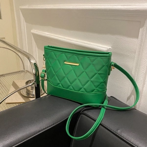 Green quilted shoulder bag with gold metal trim and chain strap on a black sofa