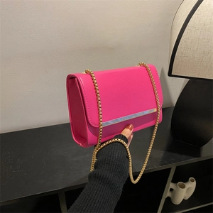 Bolso bandolera minimalista magenta con cadena dorada y elegante ribete metálico