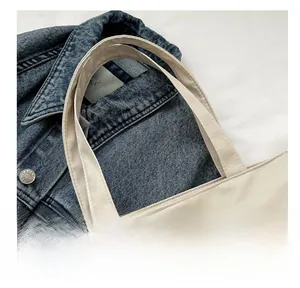 Nahaufnahme der verstärkten Nähte an beigen Canvas-Taschengriffen mit Denim-Hintergrund