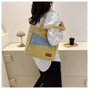 Detail of oxford fabric tote bag featuring yellow and blue color-block design and fashion label