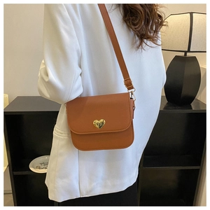 Petit sac carré marron avec fermoir cœur doré porté sur une veste de tailleur blanche