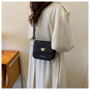 Détail du sac à bandoulière noir avec fermoir cœur doré porté sur un trench-coat beige