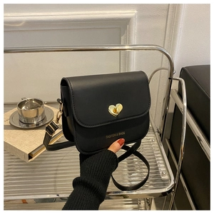 Détail du sac bandoulière en cuir mat noir avec fermoir rotatif doré en forme de cœur