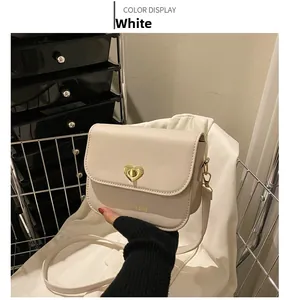 Détail du sac bandoulière blanc avec fermoir rotatif coeur doré et lettrage sur le devant