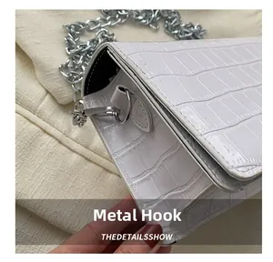 Close-up of the silver metal hook and croc-effect leather texture on a white shoulder bag