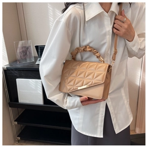 Sac bandoulière beige matelassé avec boucle dorée et anse plissée dans un décor de bureau