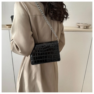 Detailed view of a black crocodile-patterned crossbody bag with silver chain on a model
