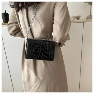 Detail of black crocodile texture small square bag with shiny silver chain strap
