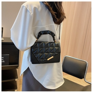Sac à main matelassé noir avec bordure dorée et anse plissée porté par un mannequin