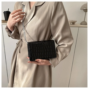 Detail of black faux crocodile skin handbag with silver chain strap on a trench coat