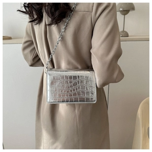Close-up of silver croc-embossed square bag with metallic chain strap on model