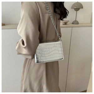Detail of silver crocodile-embossed mini square bag with metallic chain on trench coat