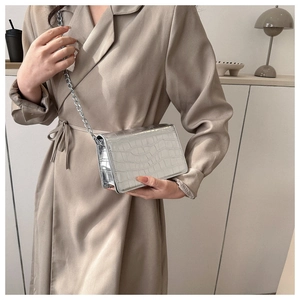 Model wearing a silver crocodile-patterned crossbody bag with a metal chain strap