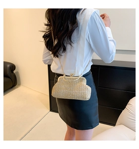 Detail of beige straw crossbody bag with gold chain strap on a model with white shirt