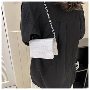 On-body view of a white crocodile pattern crossbody bag with a silver chain strap