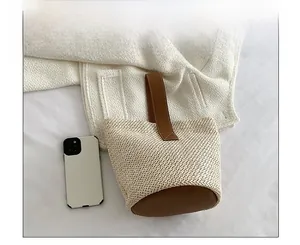 Detail of woven straw bucket bag with brown leather handles and size reference phone