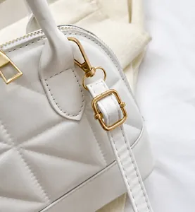 Close-up of white quilted shell bag with light gold metal hardware and adjustable strap