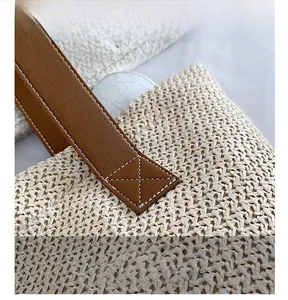 Close-up of the woven handbag featuring reinforced brown leather handles with X-stitch detailing