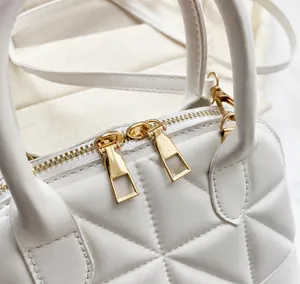 Detail of white quilted handbag showing smooth gold zippers and embossed leather texture