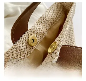 Detail of woven straw bucket bag with dark brown leather strap and gold magnetic closure