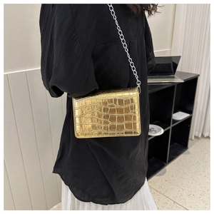 Side view of a gold crocodile embossed flap bag with a silver chain strap on a model