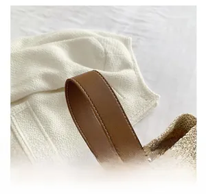 Close-up of straw woven bucket bag with brown leather handles and white stitching details
