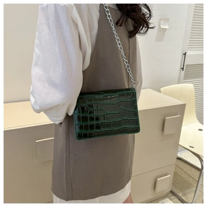 Detail of dark green crocodile texture handbag with silver chain on model outfit