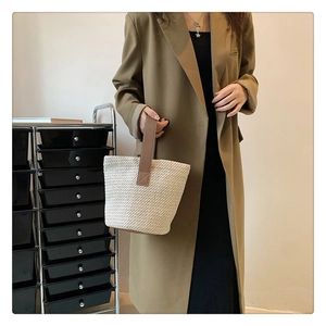 Detail of beige woven straw bucket bag with brown leather handles and reinforced stitching