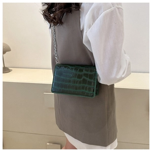 Detail of dark green crocodile texture handbag with silver chain strap on model