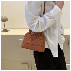 Caramel brown quilted shell bag shown on model in a minimalist interior setting