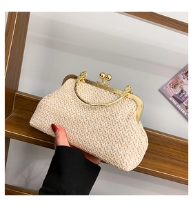 Detail of a beige woven clutch with gold metal frame and top handle held by hand