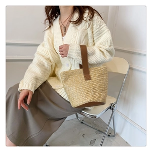 Close-up of a straw bucket bag with brown leather handles worn by a model in casual outfit