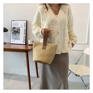 Detail of hand-woven straw bucket bag with brown leather handle in a minimalist setting