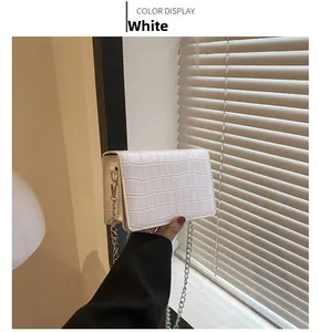 Detail of white crocodile embossed texture on a square flap bag with silver chain strap