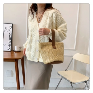 Detail of woven straw tote bag with brown leather handles held by a model in soft lighting